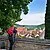 Ein Wanderer mit roten Rucksack steht an einer Mauer und lässt seinen Blick über Greding schweifen. Die Stadt ist von zwei Bäumen eingerahmt.