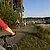 Einer Frau auf dem Rad begegnet auf einem Radweg direkt am See einer Gruppe anderer Radfahrer. Der Weg führt vorbei an Bäumen und Sträuchern sowie einem kleinen Segelhafen.