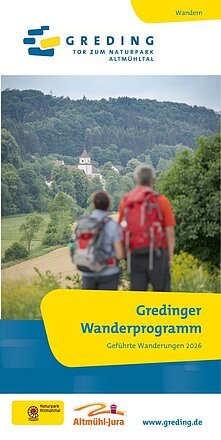 Zwei Wanderer mit Rucksäcken blicken auf eine Kirche und Wald im Naturpark Altmühltal.