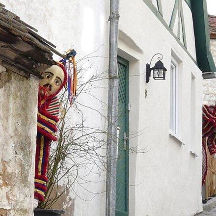 Pumpernickl Zwei Personen in bunten Kostümen und Masken schauen um Hausecken in einer gepflasterten Gasse.