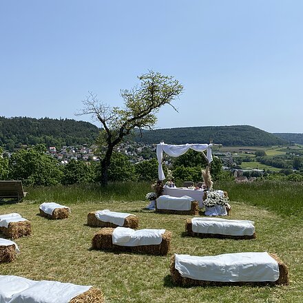 Trauung auf dem Kalvarienberg mit Strohballenbänken und weißem Stoff im Hintergrund ist Greding bei klarem Himmel.