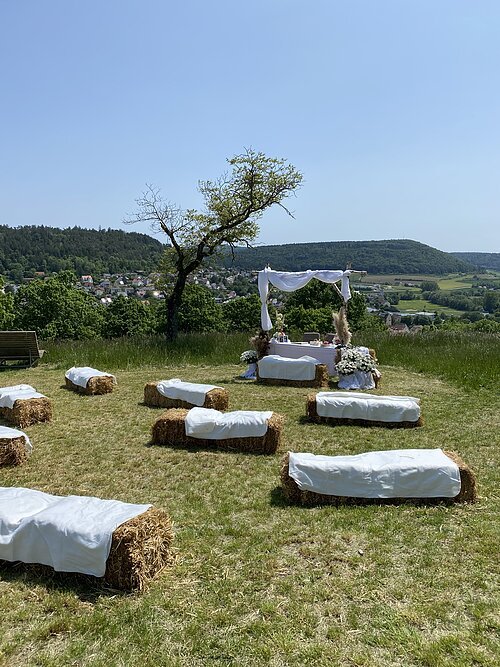 Trauung auf dem Kalvarienberg mit Strohballenbänken und weißem Stoff im Hintergrund ist Greding bei klarem Himmel.