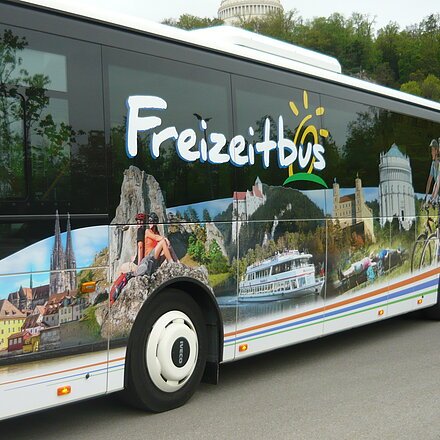 Seitenansicht eines weißen Busses mit Freizeitmotiven und dem Schriftzug „Freizeitbus“.