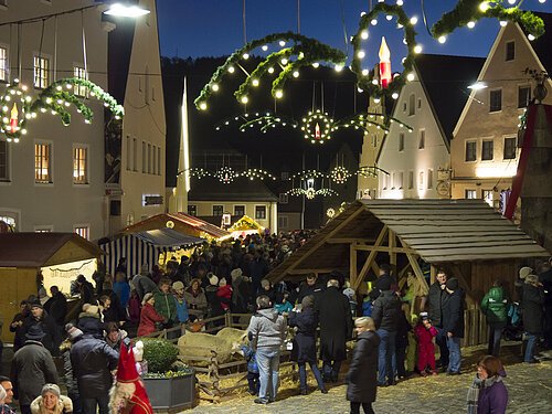 Weihnachtsmarkt mit Ständen, Menschen und festlicher Beleuchtung in einer Altstadt bei Nacht.