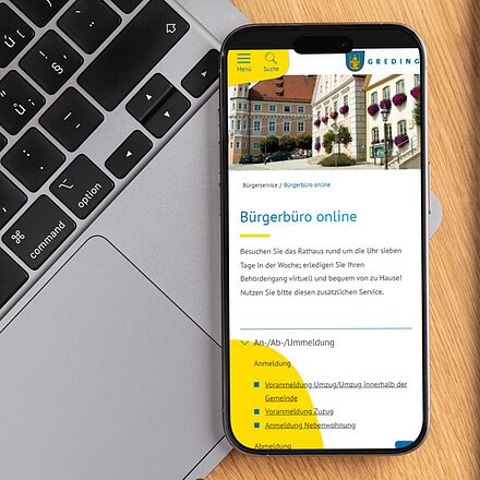 Smartphone zeigt Webseite vom Bürgerbüro online neben Laptop-Tastatur auf Holztisch