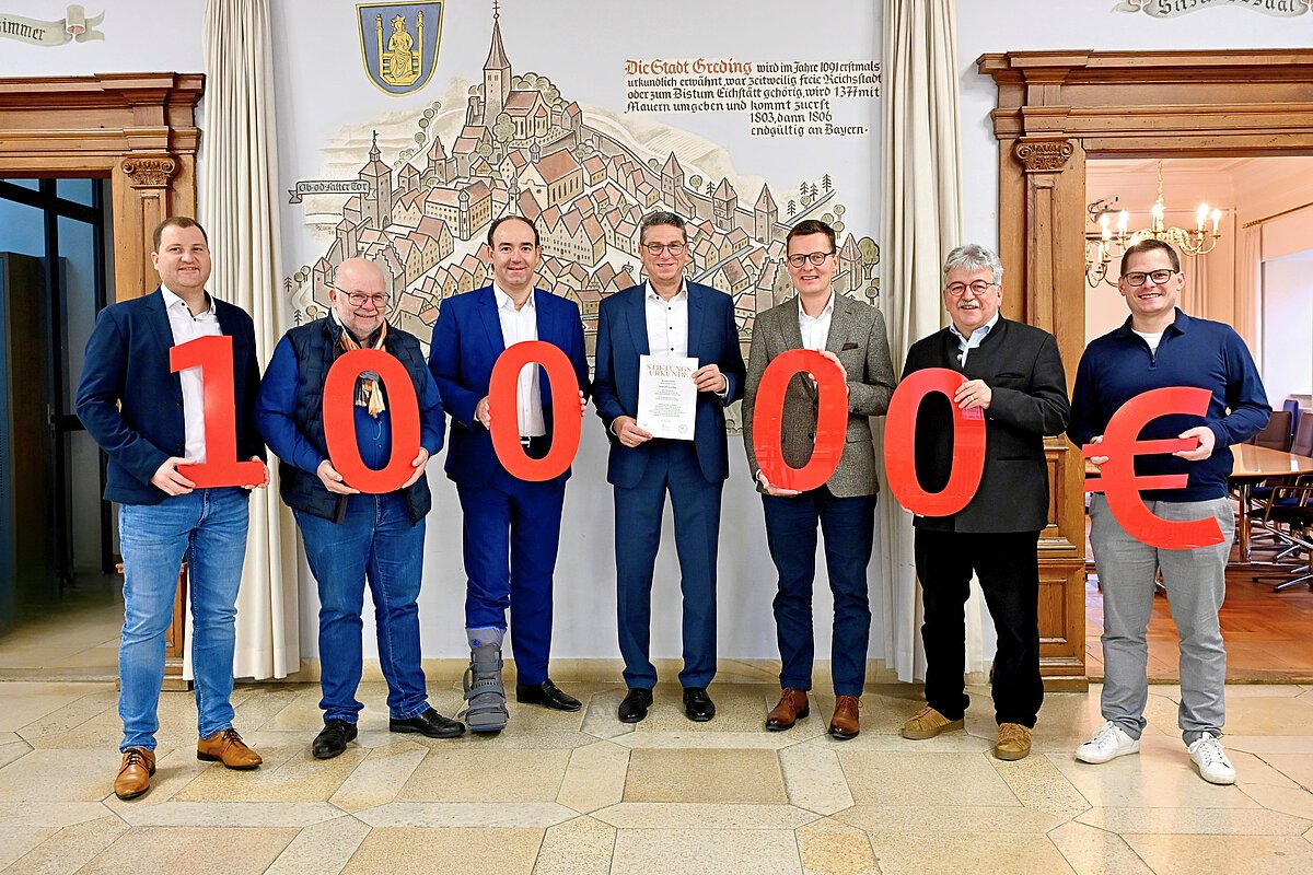 Stiftungsrat der Bürgerstiftung Greding Sieben Männer stehen in einem Raum, fünf halten rote Zahlen, die zusammen 100.000 Euro ergeben.