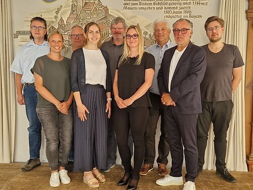 cisis 12-Zertifizierung Neun Personen stehen in zwei Reihen vor einer Wand mit historischem Wandbild und Text.