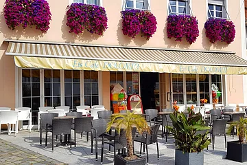Außenbereich eines Eiscafés mit Tischen, Stühlen, Pflanzen und Blumenkästen an der Fassade.