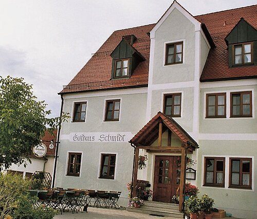 Gasthaus Schmidt, Euerwang Außenansicht eines Gasthauses mit rotem Dach, mehreren Fenstern und Sitzgelegenheiten im Freien.