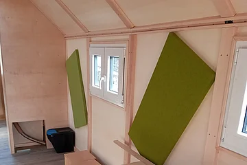 Innenraum mit hellem Holztisch, zwei grünen Schallabsorbern an der Wand und zwei kleinen Fenstern.