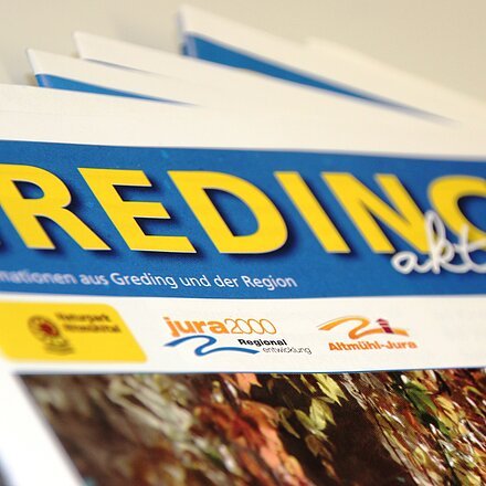 Mehrere Ausgaben der Zeitung „Greding aktuell“ mit blauem Kopf und gelbem Titel in Nahaufnahme.