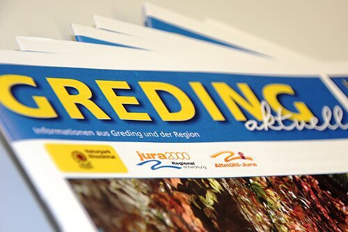 Mehrere Ausgaben der Zeitung „Greding aktuell“ mit blauem Kopf und gelbem Titel in Nahaufnahme.