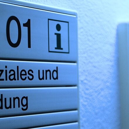 Türschild mit der Aufschrift „B 01 Soziales und Bildung“ an einer Wand in einem Gebäude