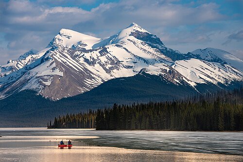 Pascal Violo Kanada & Alaska Zwei Personen in einem roten Kanu auf einem See vor schneebedeckten Bergen und einem Nadelwald.