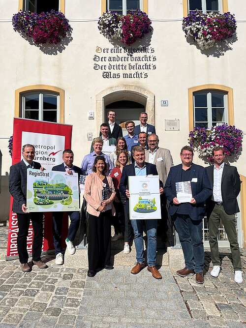 Gruppenfoto von 15 Personen vor einem Gebäude mit Blumenkästen und Bannern der Metropolregion Nürnberg.